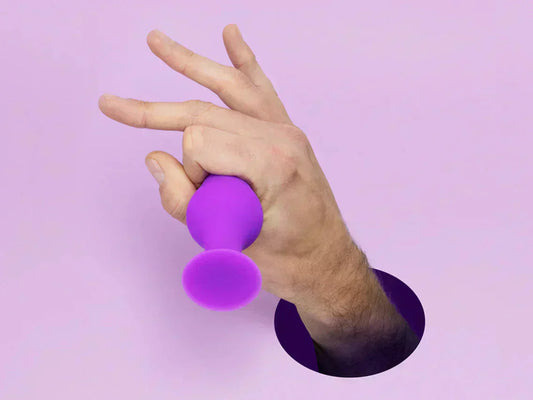 Mano sosteniendo un tapón anal morado contra un fondo lila, representando la correcta manipulación y uso de juguetes anales.